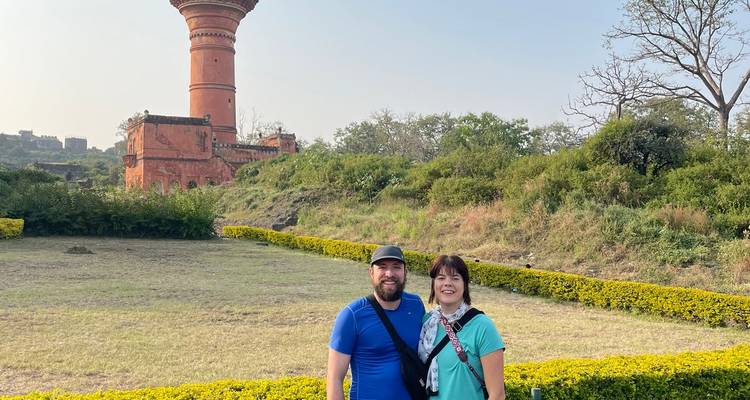 Two people standing in a garden with an ancient tower in the background.