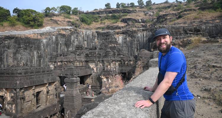 Person leaning on a wall overlooking ancient rock-cut architecture.