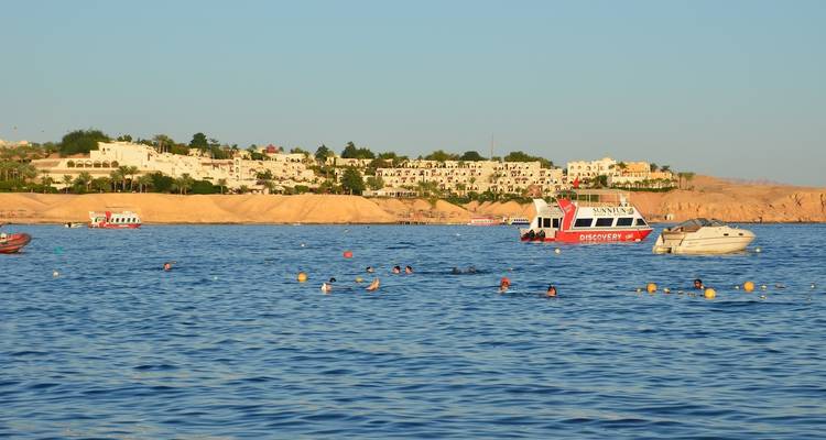 Boats and people swimming in a coastal area with resorts.