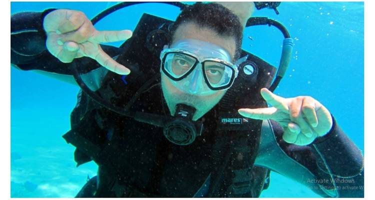A person scuba diving underwater showing peace signs.