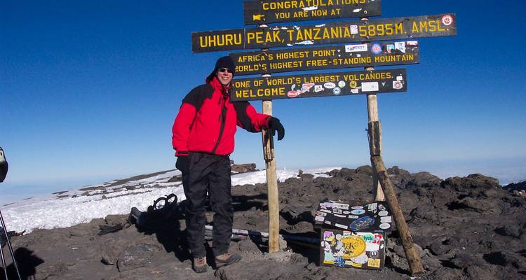 Persoon poseert bij Uhuru Peak met topborden.