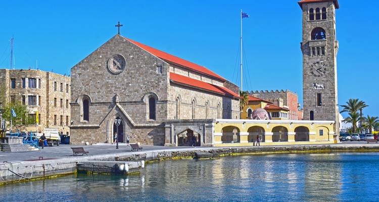 Una iglesia frente al mar con un campanario bajo un cielo azul despejado.