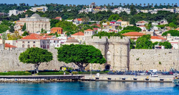 Muralla de fortaleza medieval con exuberante vegetación y vista al mar.