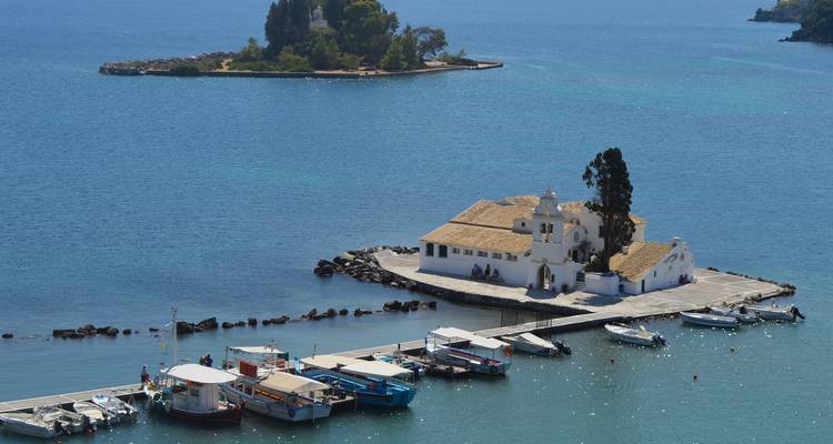 Una pequeña iglesia blanca en una isla diminuta en el mar con barcos alrededor.