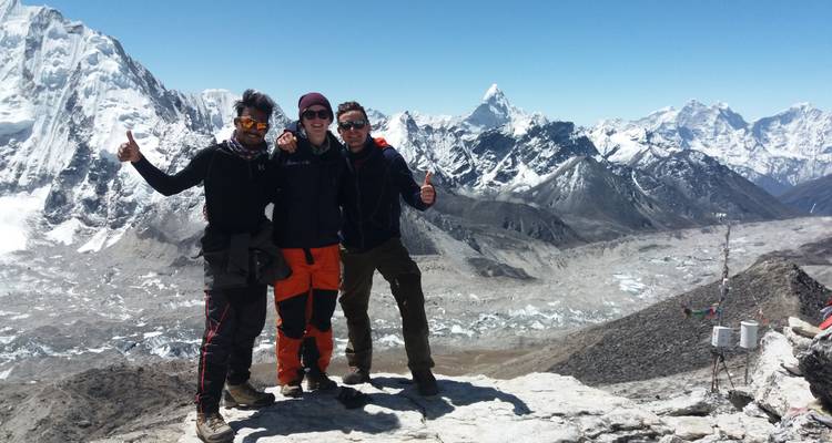 Two people giving thumbs up with mountain peaks behind.