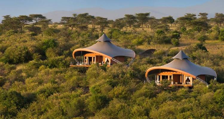 Zwei luxuriöse Zeltlodges in einer üppig grünen Gegend vor der Kulisse offener Ebenen.