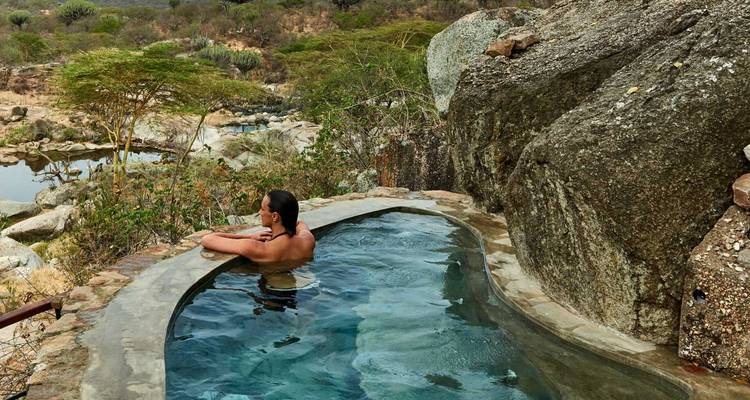 Person entspannt sich in einem Felstümpel mit malerischem Blick über die Landschaft.