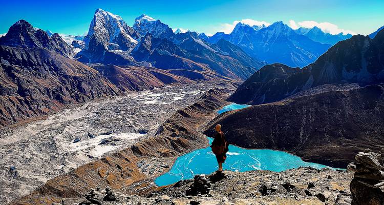 Person standing on a ridge overlooking mountain range and turquoise lakes.