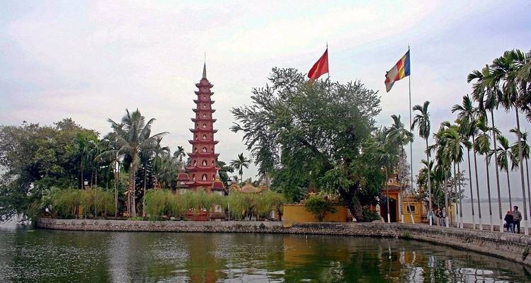 Complexe de temples au bord d'un lac avec des drapeaux et une végétation luxuriante.