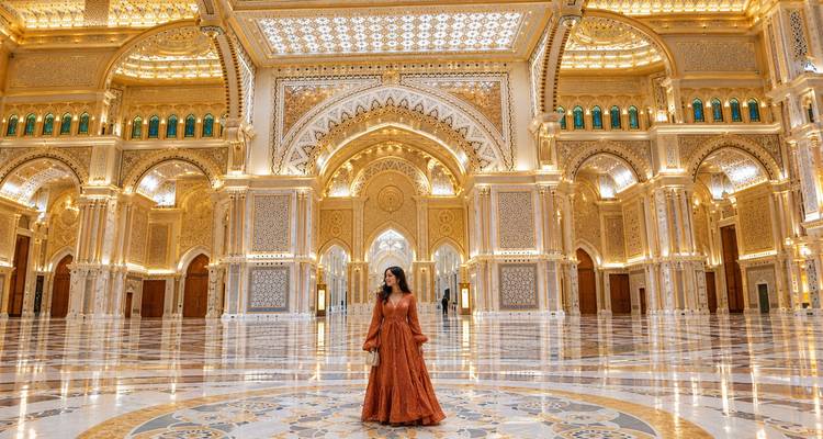 Elegant geklede vrouw staat alleen in de glinsterende marmeren hal van het Qasr Al Watan paleis, omgeven door gouden bogen en kroonluchters.