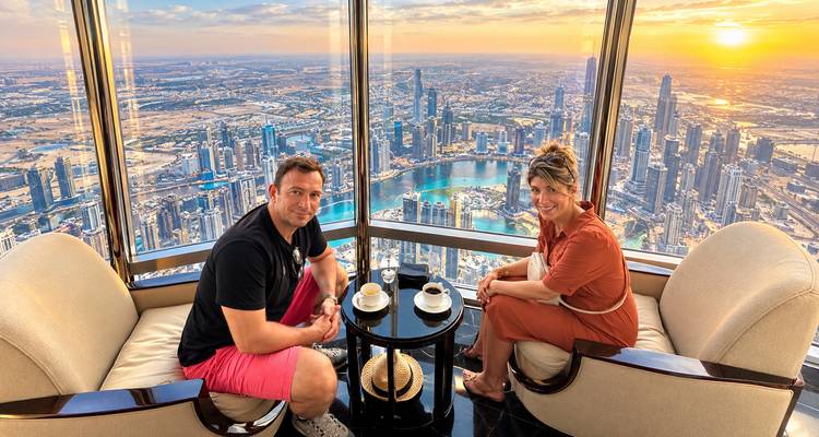 Un couple savourant un café dans un salon d'un immeuble de grande hauteur surplombant l'horizon de gratte-ciel de Dubaï au coucher du soleil.