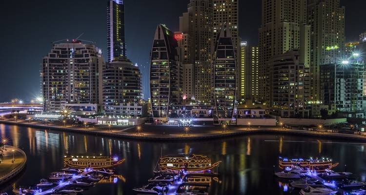 Dubai Marina skyline illuminated at night with boats in the water.