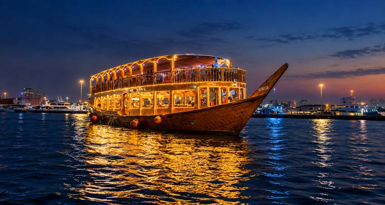 Restaurant traditionnel en dhow en bois illuminé de lumières chaleureuses naviguant sur des eaux calmes au crépuscule