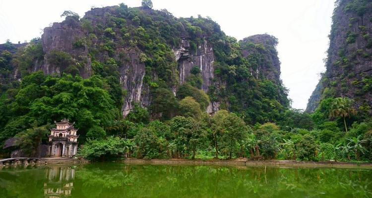 Kalksteinfelsen, die sich über einen kleinen historischen Tempel und einen grünen Teich in einem üppigen Tal erheben