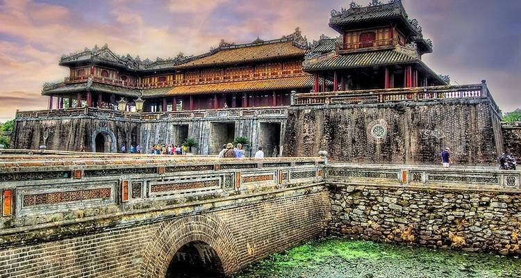 Dramatisches HDR-Bild der Mauern und Brücke der Zitadelle von Hue bei Sonnenuntergang mit kleinen Figuren auf den Wällen