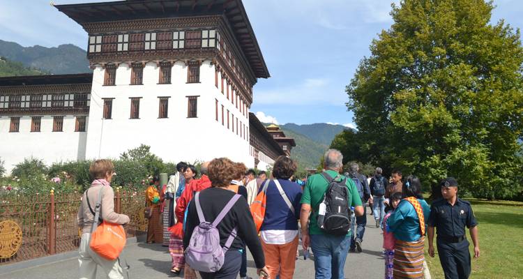 Tourists in traditional and modern attire exploring a Bhutanese site.