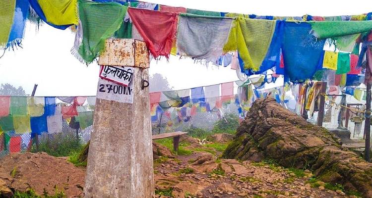 Gebetsfahnen mit einem Steinmarker, der die Höhe anzeigt, und schneebedeckte Berge im Hintergrund.