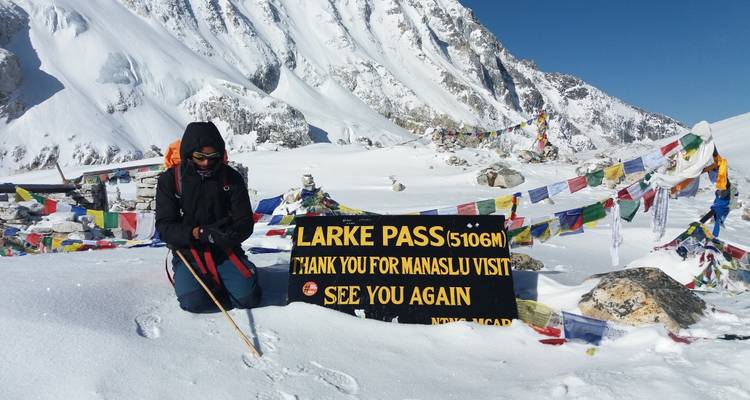 Persoon bij Larke Pass in besneeuwde bergen met gebedsvlaggen.