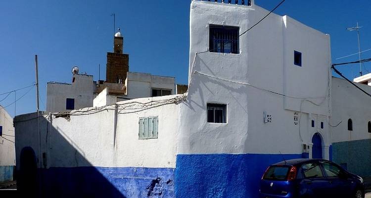 Bâtiment peint en bleu et blanc avec une voiture garée à côté.