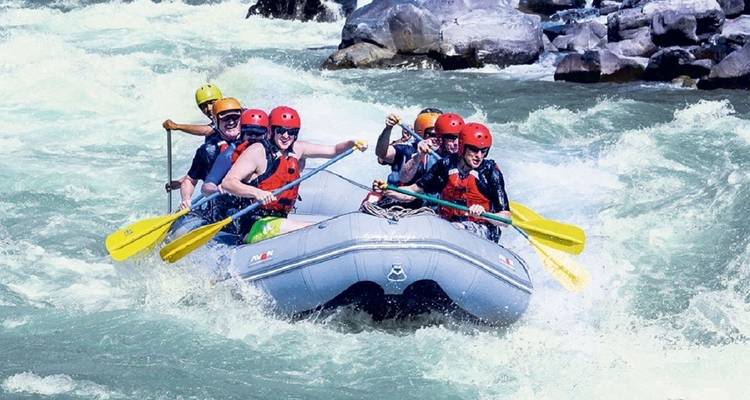 Group rafting with paddles raised against white-water rapids.