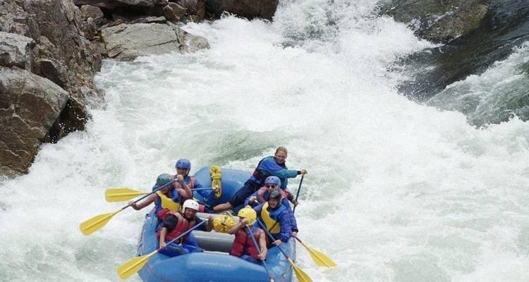 Group of people rafting down a rough white-water rapid.