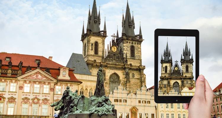 A street view in Prague featuring a historic church and a tourist using a tablet.