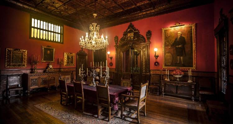 Lujoso comedor colonial con lámpara de cristal, paneles de madera noble y retratos antiguos.