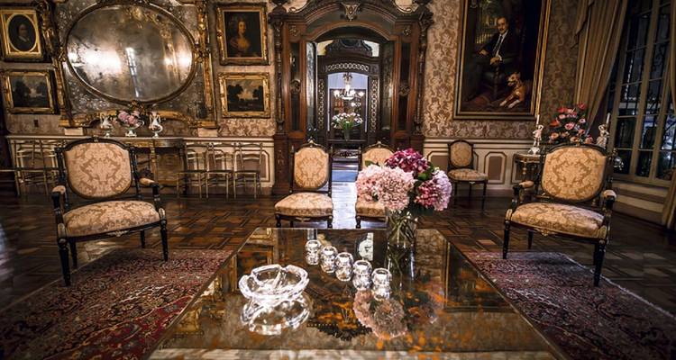 Lujoso salón adornado con cuadros antiguos, espejos ornamentados y muebles mullidos en un museo de mansión limena.