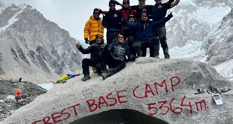 Triumphale Trekker stehen auf dem berühmten Stein mit der Markierung Everest Base Camp 5364m, dahinter der Khumbu-Eisbruch.