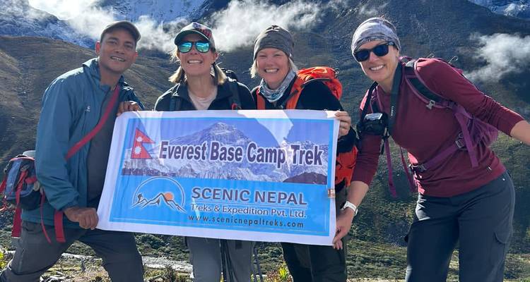 Kleines Trekking-Team lächelnd mit Everest Base Camp Trek Banner inmitten alpiner Landschaft.