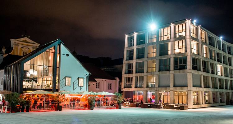 Complexe hôtelier et gastronomique moderne illuminé la nuit avec un espace de détente extérieur chaleureux.