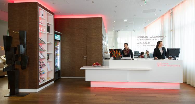 Hall de réception d'hôtel lumineux avec deux membres du personnel derrière un bureau blanc épuré accueillant les clients.