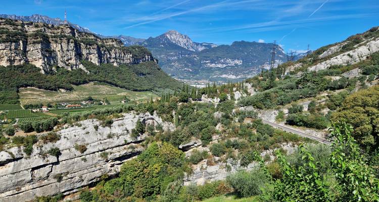 Wide alpine valley with dramatic limestone cliffs, green fields, and distant peaks under blue sky.