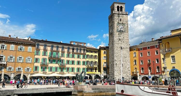 Busy waterfront square in Riva del Garda with tall stone clock tower and colorful facades.