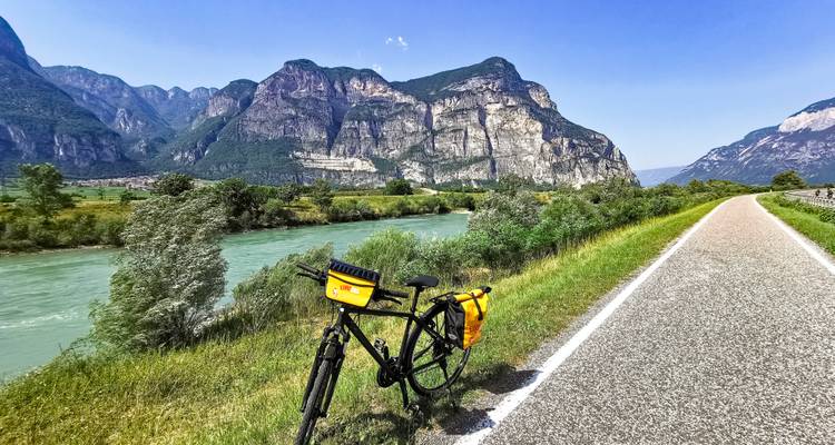 Un vélo de randonnée solitaire repose à côté d'une rivière turquoise sur une piste cyclable pittoresque bordée de falaises imposantes.