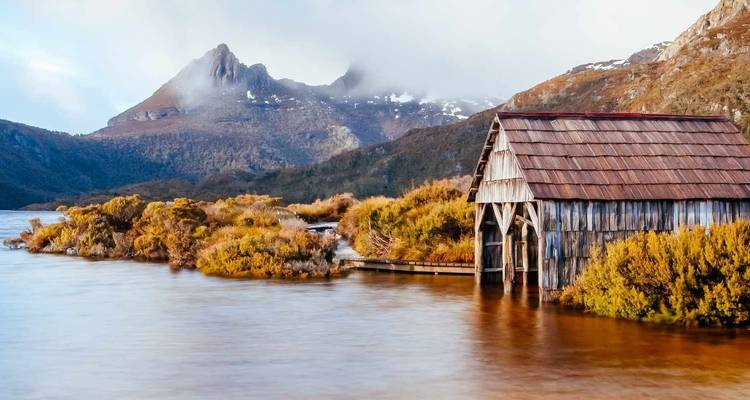 Ruhiger See mit einem hölzernen Bootshaus und Bergkulisse.