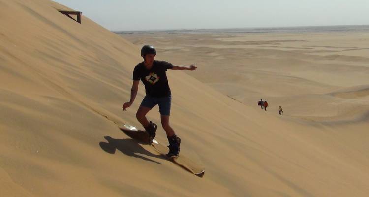 Homme faisant du sandboard sur une grande dune de sable.