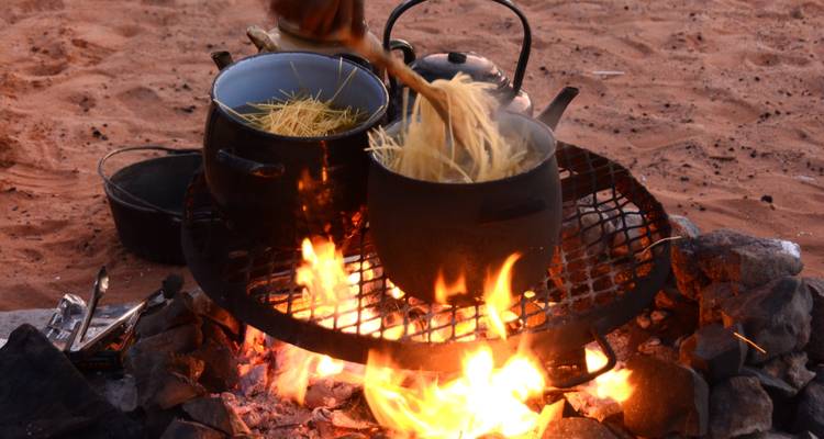 Marmites suspendues au-dessus d'un feu de camp dans un environnement désertique.