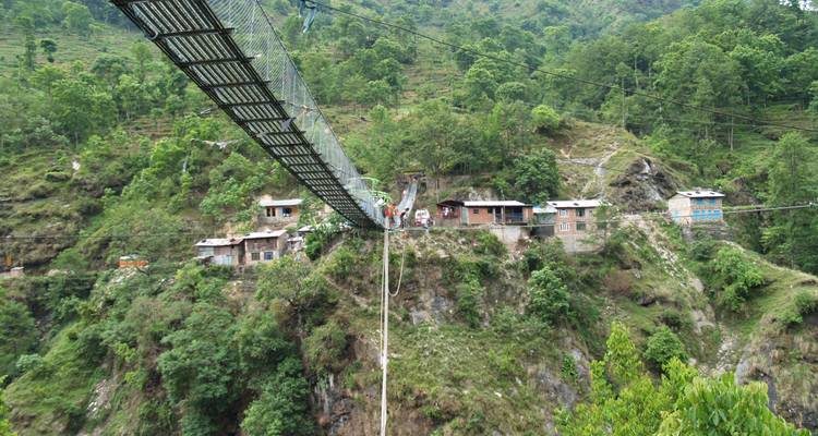 Suspension bridge over a lush valley with small houses.