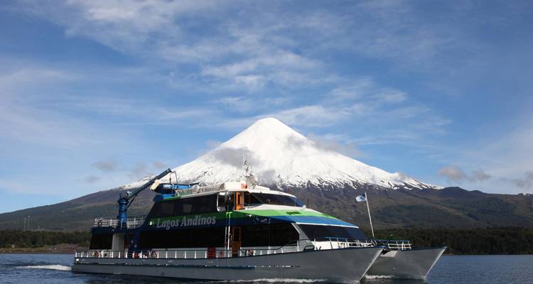 Gran barco navegando con un volcán cubierto de nieve al fondo.