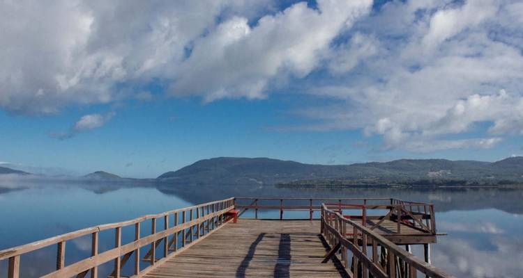 Una terraza de madera que se extiende sobre un lago tranquilo con un cielo despejado.