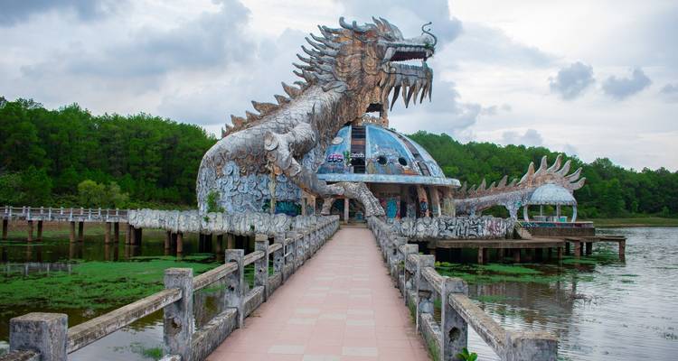 Dragon-shaped ruin of Hue’s abandoned water park reached by a tiled walkway over a lily-filled lake.