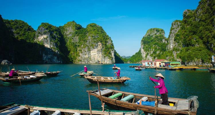 Locals rowing traditional boats among dramatic limestone islands in Ha Long Bay under a clear sky.