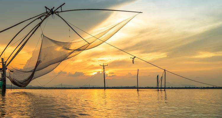 Silhouetted traditional fishing nets spanning calm river at golden sunset.