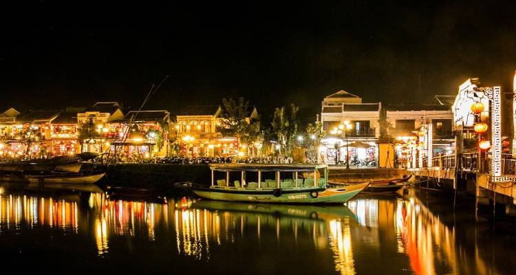 Lantern-lit boats and historic shophouses reflected in the calm river of Hoi An’s Ancient Town at night.