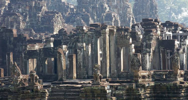 Weathered stone pillars and crumbling galleries of the Bayon temple complex in morning haze.