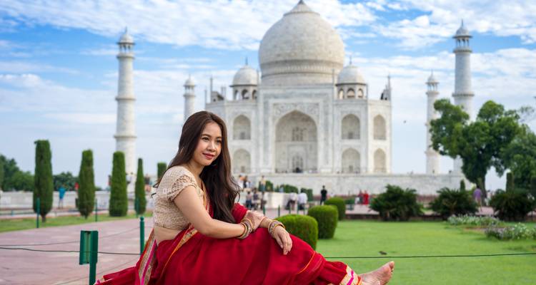 Mujer joven en sari tradicional posando descalza frente al Taj Mahal en un día brillante.