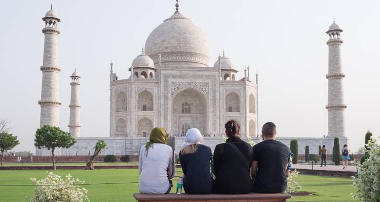 Cuatro viajeros sentados en un banco admirando la fachada de mármol del Taj Mahal.