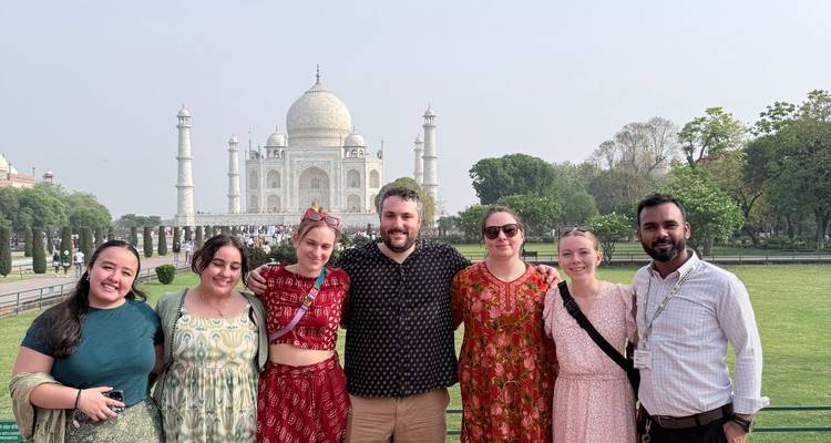 Grupo de viajeros felices posando juntos con el Taj Mahal detrás de ellos en una mañana brumosa.