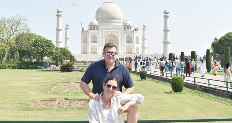 Couple poses in front of the Taj Mahal gardens with crowds behind them on a sunny day.